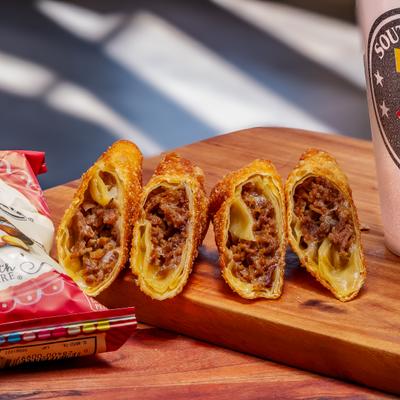 Egg rolls on a wooden board beside a bag of chips.