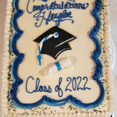 Graduation cake, blue icing text, a black grad cap and diploma icing decorations.