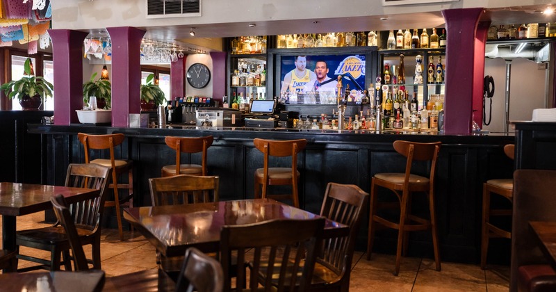Interior of a bar with wooden furniture, a variety of liquor bottles, and a TV