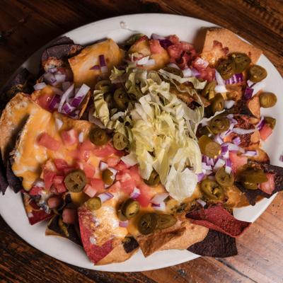 Nachos topped with with melted cheeses,  tomatoes, onions, jalapeños, lettuce, salsa, and sour cream.
