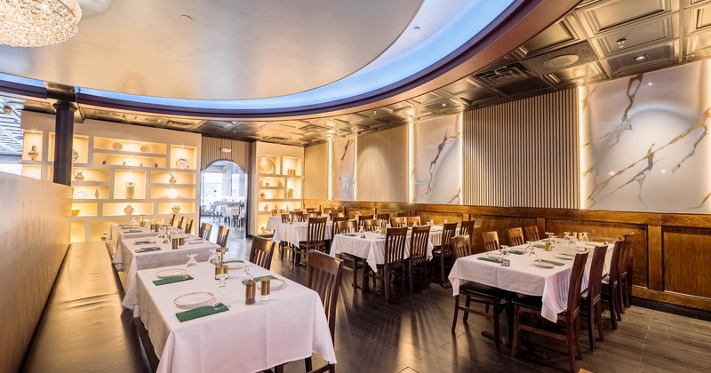 Elegant restaurant dining area with white tablecloths, wooden furniture, marble-themed walls