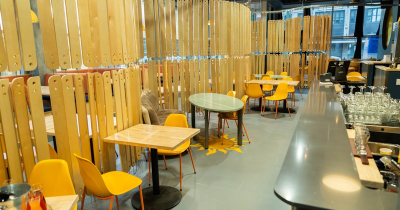 A modern dining area with wooden tables, yellow chairs, and vertical wooden slat partitions