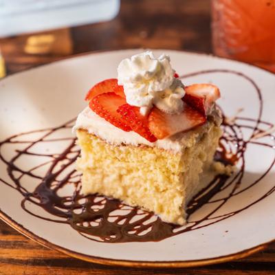 Moist Tres Leches cake slice topped with fresh strawberries and whipped cream.