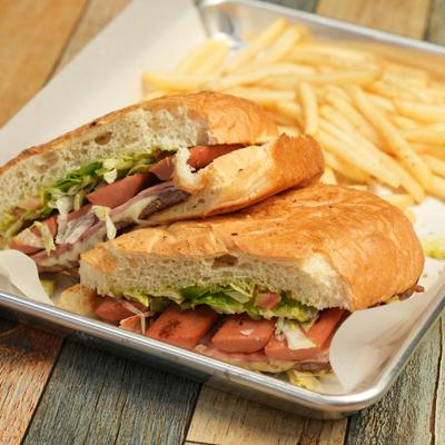 Torta sandwich filled with sliced hot dogs, lettuce, and tomatoes, served with fries.