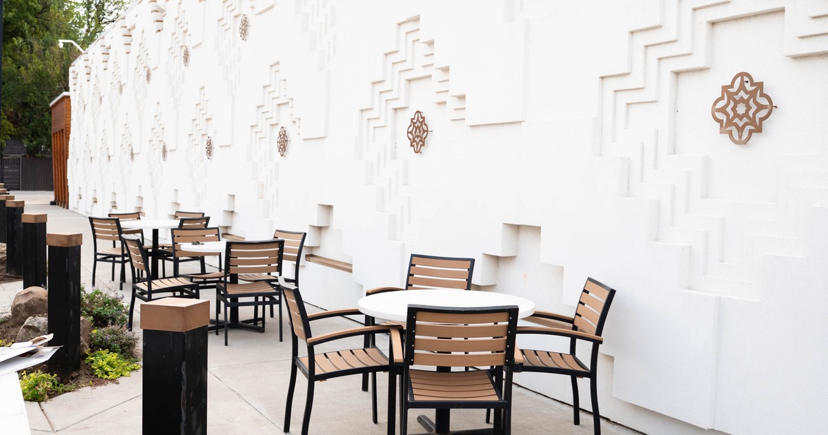 Outdoor patio with round tables and wooden-slat chairs beside a white