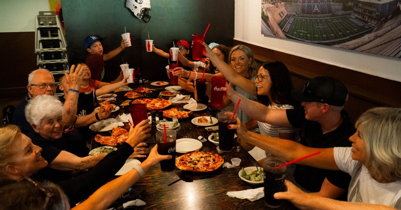 A group of people socializing over pizza and beverages at a table inside