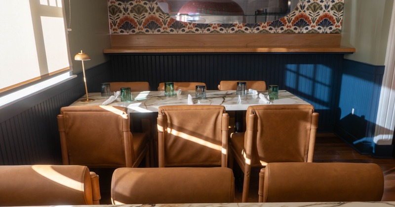 Dining area with a marble table, tan leather chairs, floral wallpaper