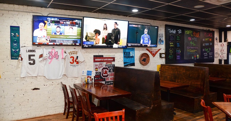 Interior, tables, chairs and wooden high back benches, tv screens on the wall