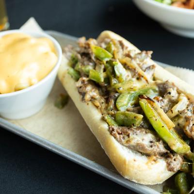 Philly cheesesteak served with a bowl of mac and cheese.