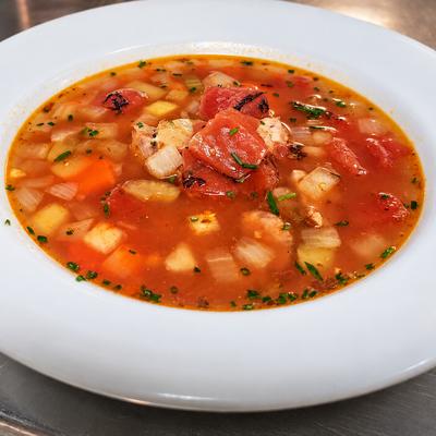 A bowl of tomato-colored soup with vegetables and herbs on the pub counter..