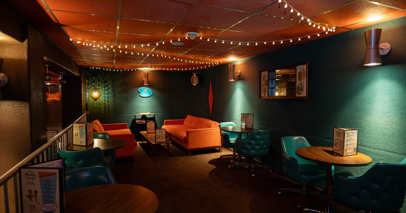 Inside, cozy lounge with turquoise walls, orange ceiling tiles, aqua chairs, wooden tables