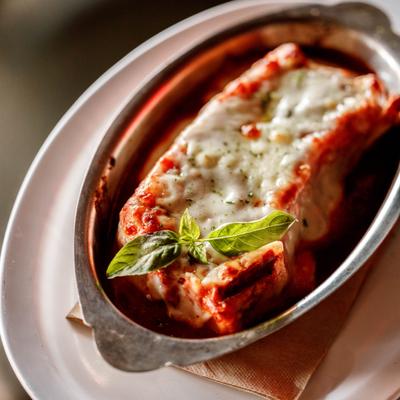 Lasagna packed with meat and cheese, covered in red sauce, garnished with basil.