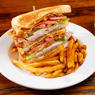 Club sandwich stacked with deli meats, cheese, lettuce, and tomato, served with seasoned fries.