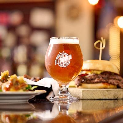 A branded glass of amber beer sits next to a large burger.