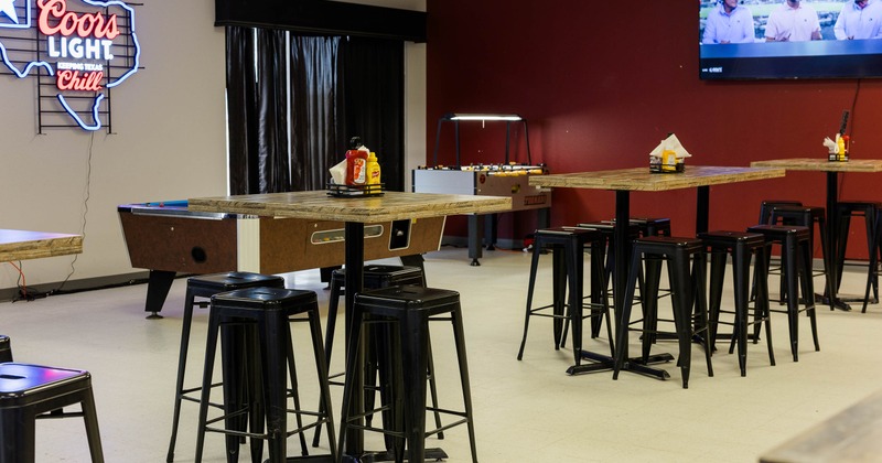 Interior - high wooden tables, metal stools, neon sign, pool and foosball tables and a TV