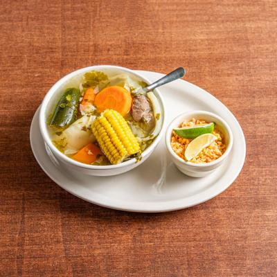Mexican beef and vegetable soup with a side of rice and lime wedges.