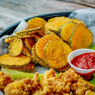 Fried pickles and fried cauliflower, on a plate with celery and a cup of red sauce.