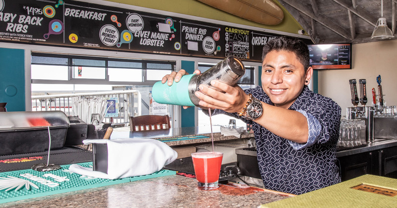 Interior, smiling bar staff pouring a drink from shaker behind counter