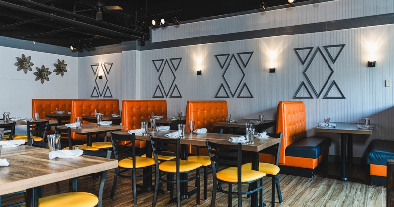 Restaurant interior, wooden tables, black chairs with yellow seats, orange booth seating, wall decor