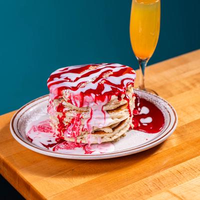 Pancake stack drizzled with strawberry and icing, served with a mimosa.