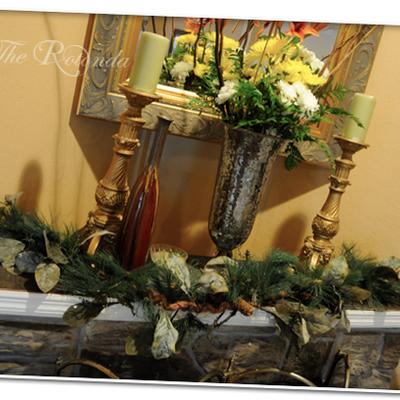 Elegant mantle display featuring gold candlesticks, a silver vase, and festive greenery.