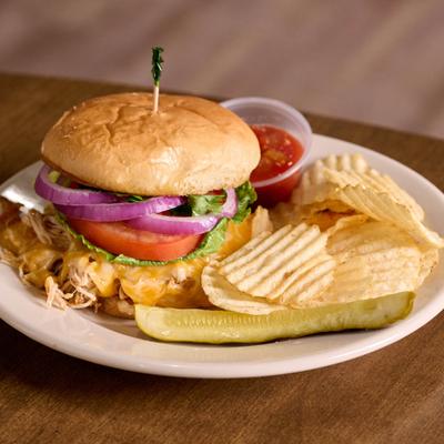 Shredded chicken taco sandwich with lettuce, onion, tomato and sides.