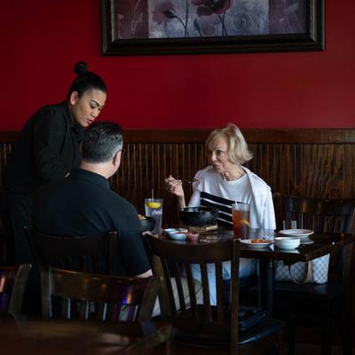 A server brings a meal to a pair of guests seated at a restaurant table.
