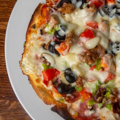 Supreme pizza topped with sausage, ham, melted cheese, olives, and peppers.