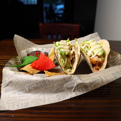 Two grilled fish tacos with corn chips.