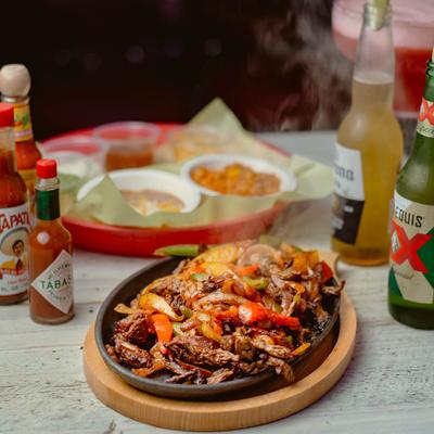 Sizzling fajitas served with sauces and beer bottles