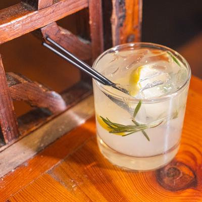 Cocktail in a rocks glass, garnished with a lemon peel and rosemary spring.