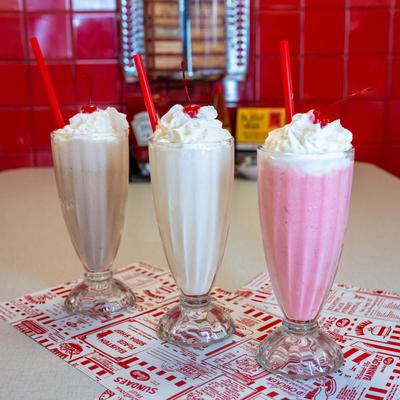 Chocolate, vanilla, and strawberry milkshakes with whipped cream and cherries.