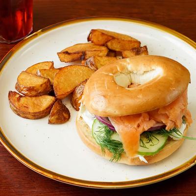 Smoked salmon bagel with cucumber, onions, cream cheese, and dill, served with roasted potatoes.