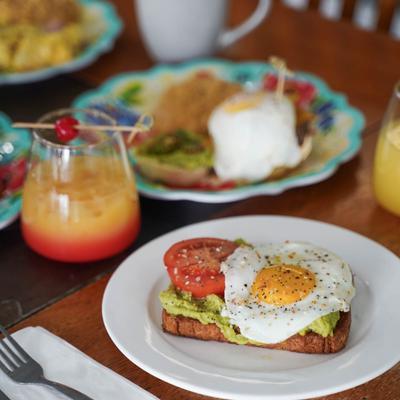 Avocado toast topped with a fried egg, served with a cocktail and other dishes.