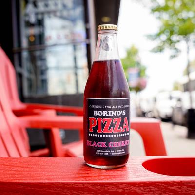 A bottle of black cherry soda with Borino's Pizza label, sits on a red chairs outside.