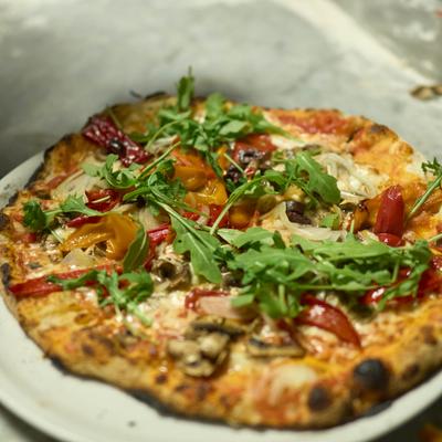 Pizza topped with fresh arugula, sliced peppers, mushrooms and onions.