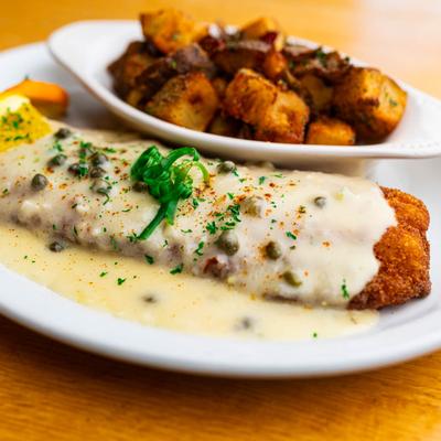 Fried walleye covered in sauce with capes, served with home fries on the side.
