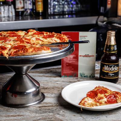 Pepperoni pizza on a metal stand beside a served slice and a bottle of beer.
