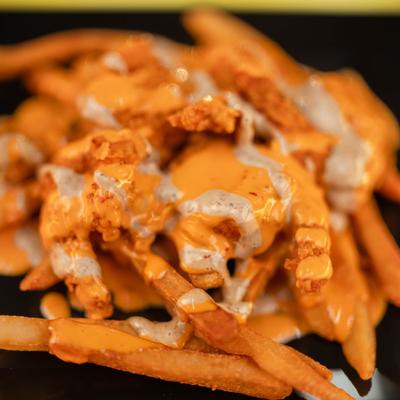 Loaded shrimp fries drizzled with sauces, close-up.