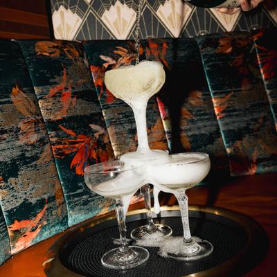 A bottle of champagne is pouring into a pyramid of coupe glasses.