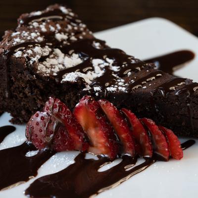 Chocolate Torte slice topped with powdered sugar and chocolate drizzle, strawberry garnish.