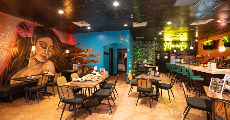 Cozy interior dining area with a large mural of a woman on the wall and a bar area on the right side