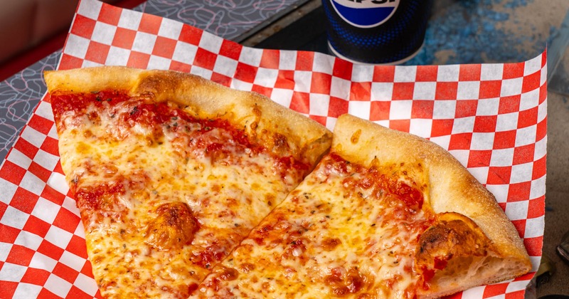 Cheese pizza slices served beside a soft drink