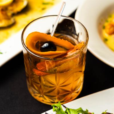 Old Fashioned cocktail with orange peel and cherry garnish.