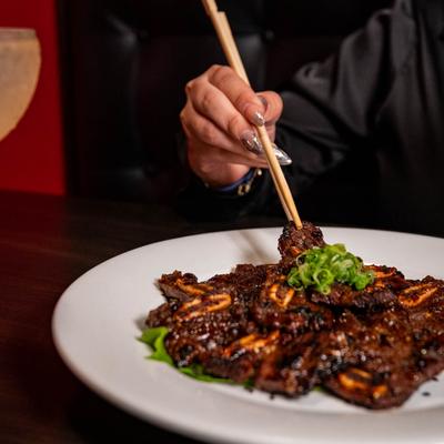 A person is enjoying marinated grilled short ribs at a table.