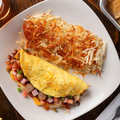 Omelet with meats, tomatoes, onions, green peppers, mushrooms, cheese, and hash browns.