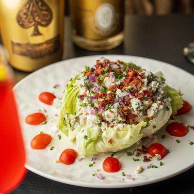 Wedge salad with bacon bits, blue cheese crumble, and cherry tomatoes on a white plate.