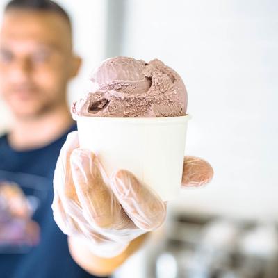 Gelato cup held in front of the camera with blurred server in the background.