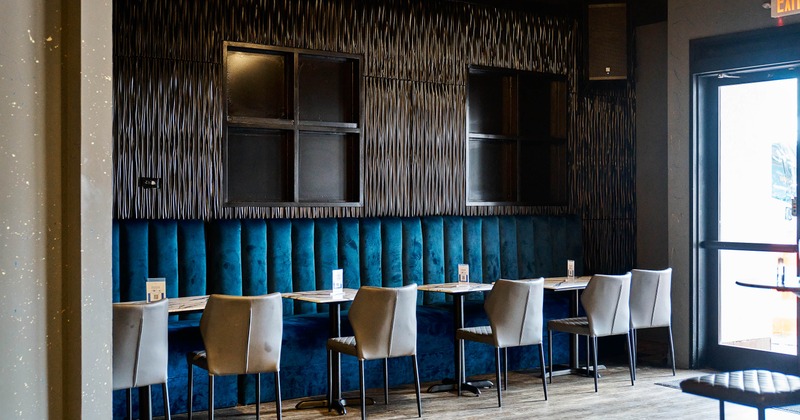A modern dining area with blue velvet booth seating, gray chairs