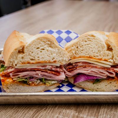 A sandwich with layers of ham, salami, lettuce, onion, and cheese.